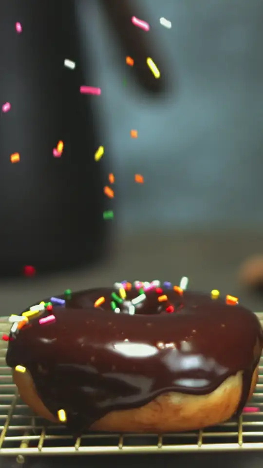 Donut de chocolate recebendo granulado colorido